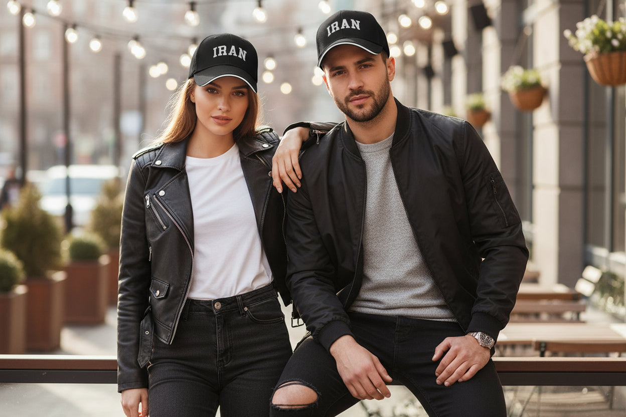 Two people wearing black caps with 'IRAN' printed on them, standing outdoors.