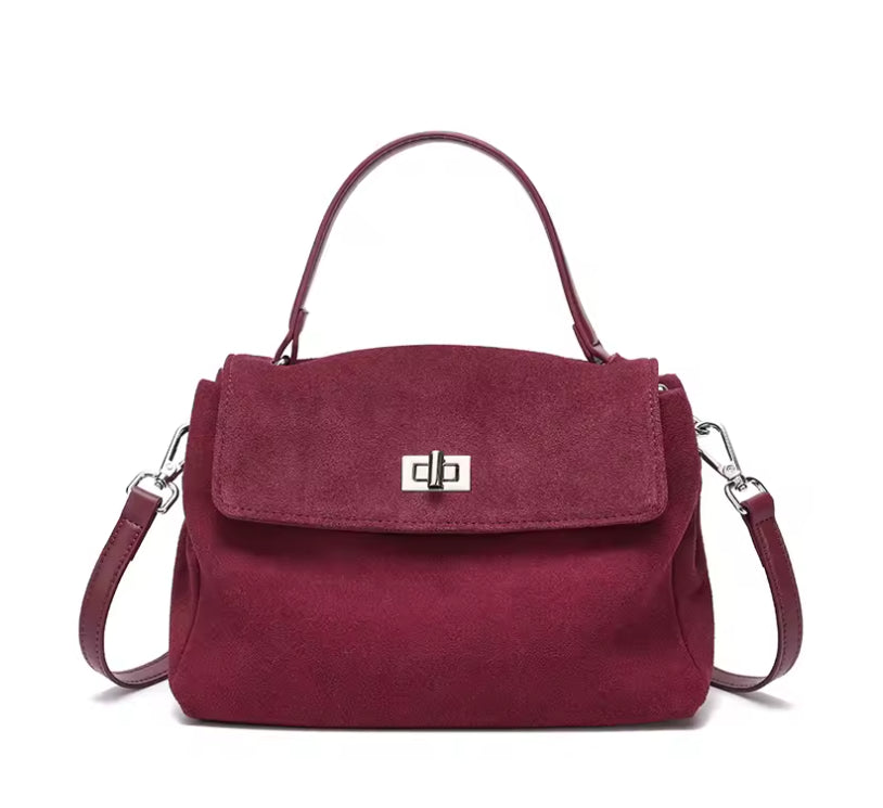 A burgundy suede handbag with a top handle, a detachable shoulder strap, and a silver-tone metal clasp on the front flap, shown against a plain white background.
